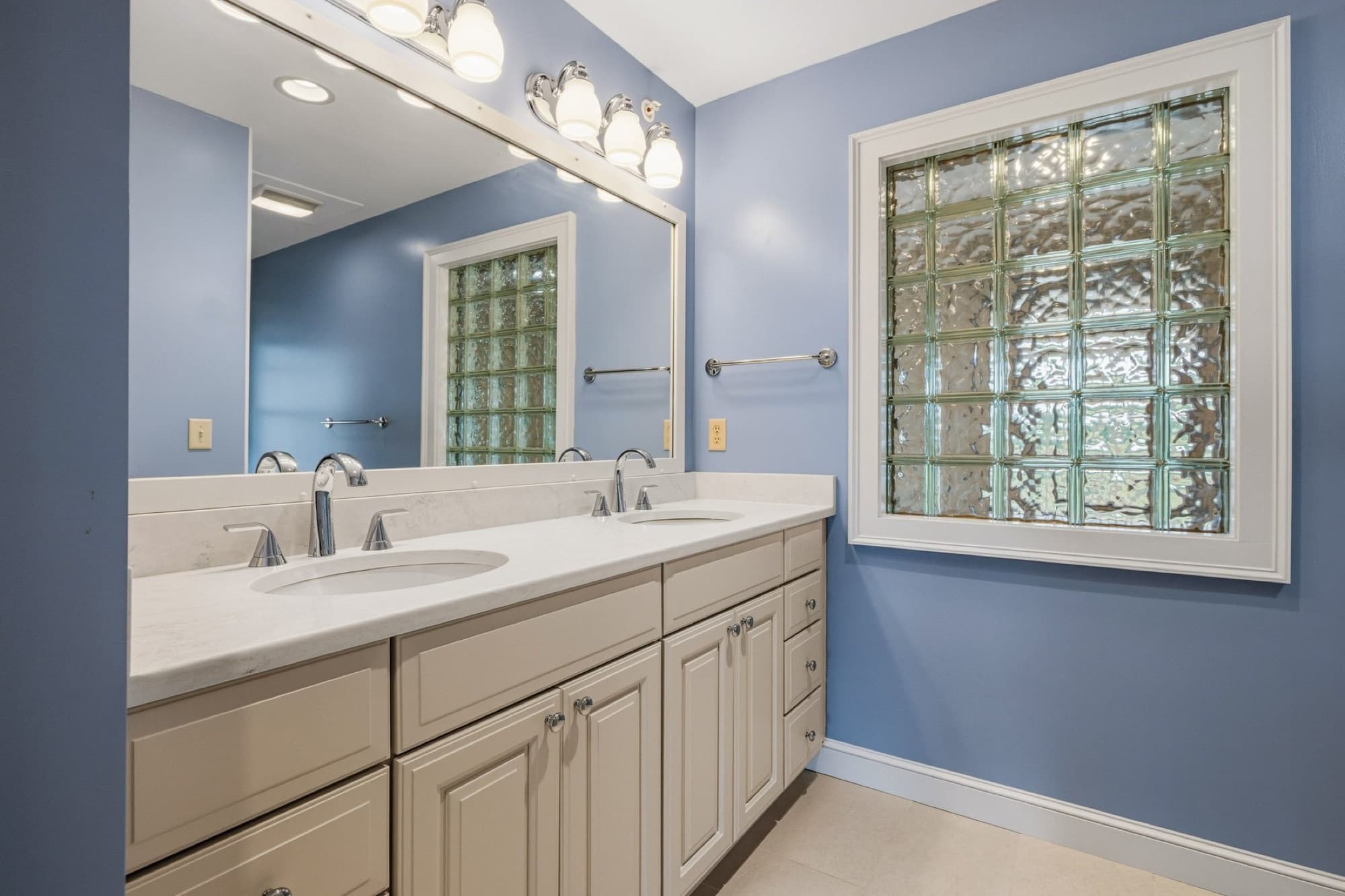 The renovated primary bath with a double vanity and a glass block window