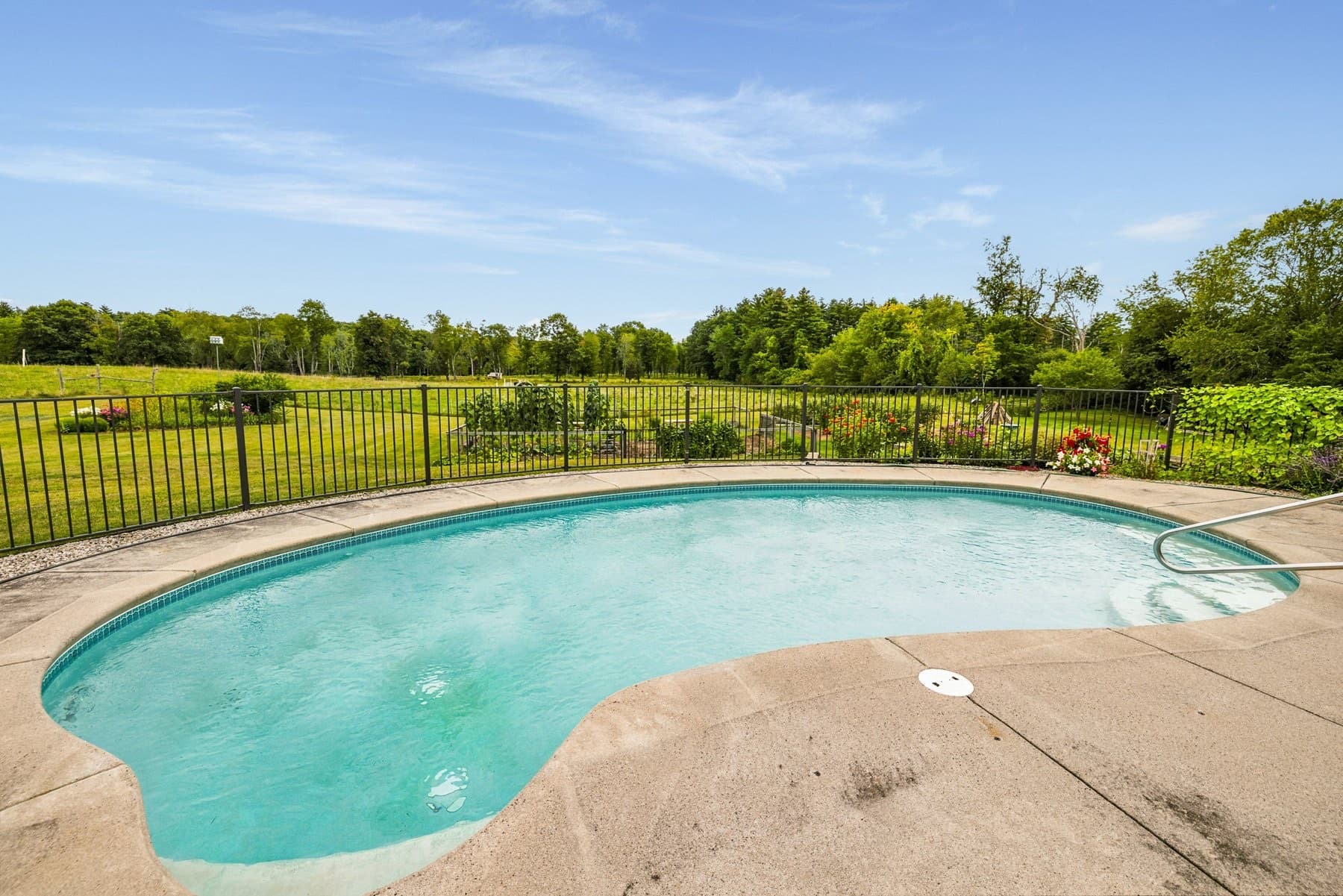 The fenced Gunite pool with the open fields and tree line beyond
